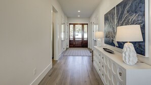 Un pasillo con piso de madera, una consola blanca con lámpara y un cuadro abstracto grande en la pared.