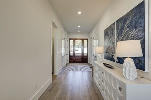 A hallway with a wooden floor, a white console table with a lamp, and a large abstract painting on the wall. - 83 Dune Lane - Oceanfront Gem- Discover this NEW 7-Bedroom Haven (Hilton Head Island)