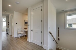 A hallway with wooden flooring, white doors, a chair, a small table, and a window with a view of a house. - 83 Dune Lane - Oceanfront Gem- Discover this NEW 7-Bedroom Haven (Hilton Head Island)