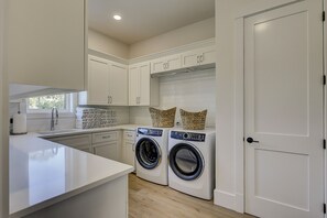 A modern kitchen with a built-in washing machine and dryer, white cabinetry, and a window. - 83 Dune Lane - Oceanfront Gem- Discover this NEW 7-Bedroom Haven (Hilton Head Island)