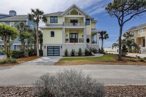 A two-story house with a front garage, a balcony, and a well-maintained lawn. - 83 Dune Lane - Oceanfront Gem- Discover this NEW 7-Bedroom Haven (Hilton Head Island)