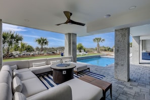 An outdoor living area with a pool, a sofa, and a ceiling fan. - 83 Dune Lane - Oceanfront Gem- Discover this NEW 7-Bedroom Haven (Hilton Head Island)