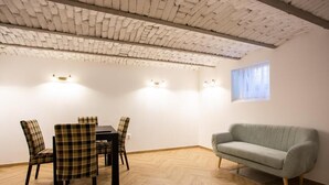 A room with a herringbone-patterned ceiling, a dining table with four chairs, a sofa, and a window with curtains.
