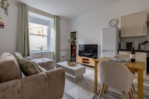 A living room with a sofa, coffee table, TV, and a small kitchen area with a refrigerator and microwave. - Stylish 1 -Bed Leith Apartment | Near Shore & Tram (Edinburgh)