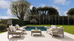 En terrasse med to sofaer og et bord, en swimmingpool og en hæk.