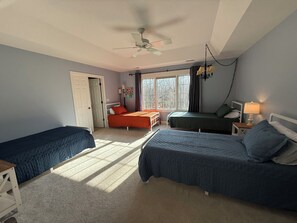 A bedroom with two single beds, a ceiling fan, a window with curtains, and a bedside table with a lamp.