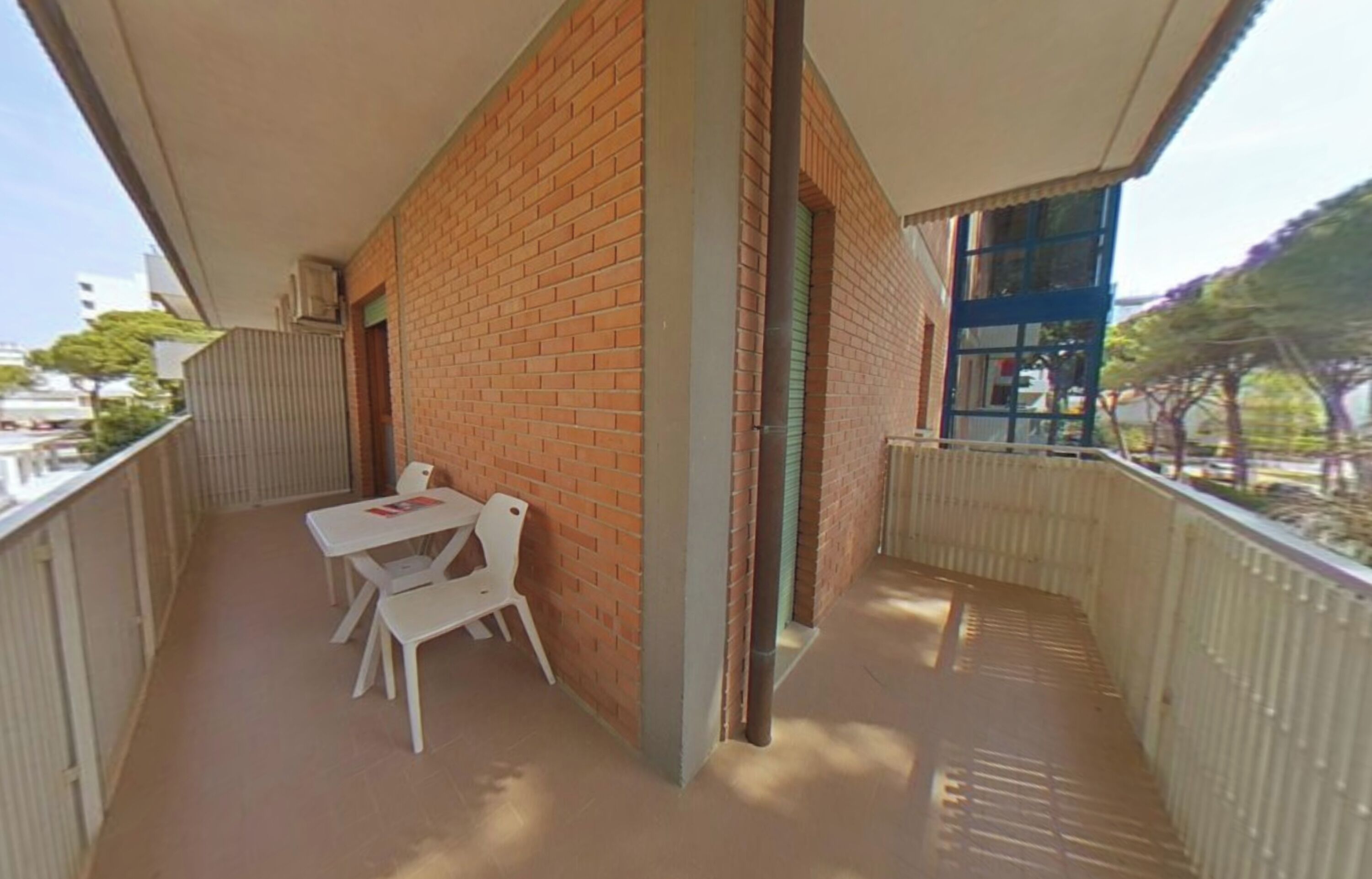 Een balkon met een witte tafel en stoelen, een bakstenen muur en uitzicht op de omgeving.