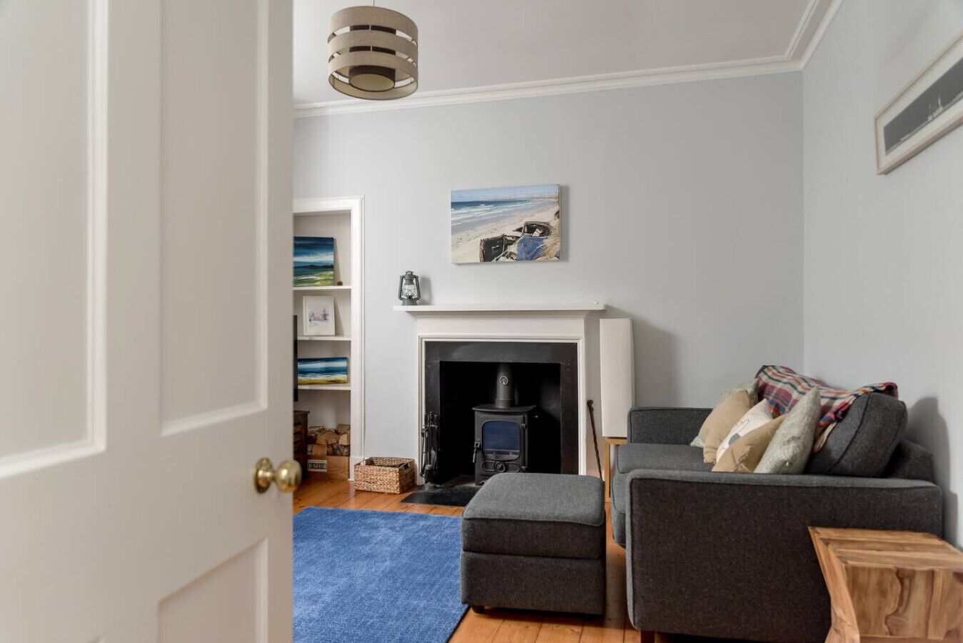 Una sala de estar con chimenea, un sofá, un tapete azul y una estantería con marcos.