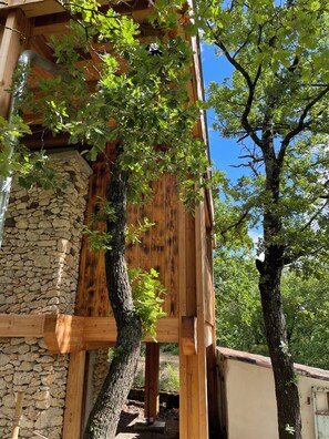A wooden structure with stone walls, a wooden beam, and a tree. - Le Nid in Provence (Le Puy-Sainte-Réparade)