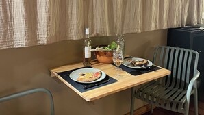 Un tavolo d'angolo con una bottiglia di vino, un bicchiere e un piatto con cibo, con il fondo sfumato da tende e un pavimento in legno.