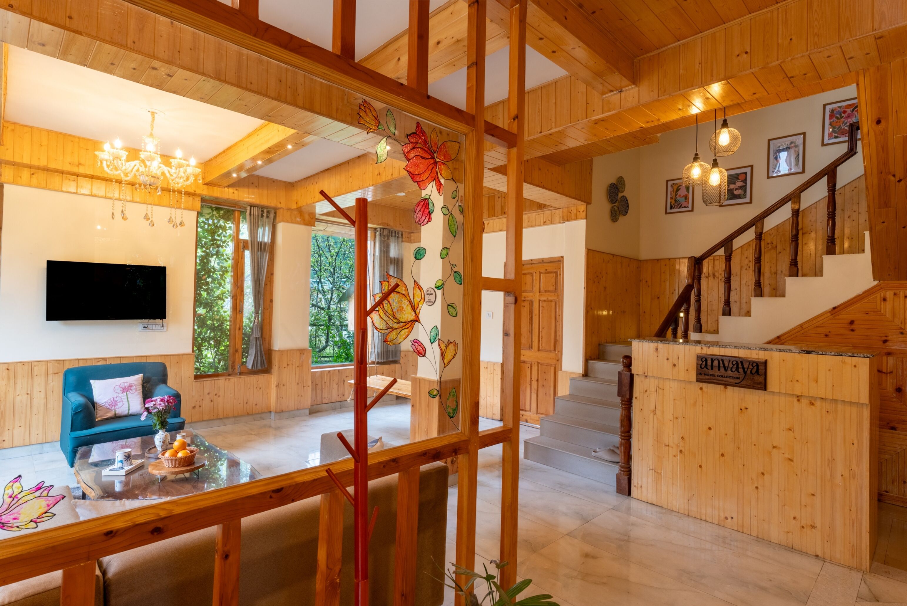 A wooden interior with a TV, a blue sofa, a dining table with fruit, and a staircase.