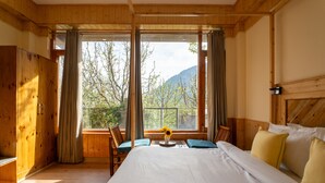 Quarto de madeira com uma cama grande, uma janela com cortinas, um guarda-roupa de madeira e vista para árvores e montanhas.