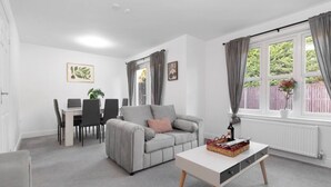 Een moderne woonkamer met een grijze bank, een witte salontafel, en een eetgedeelte met een tafel en stoelen.