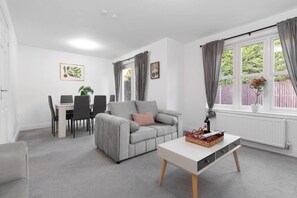 A modern living room with a grey sofa, a white coffee table, and a dining area with a table and chairs. - Buie`s Runway Retreat (Edinburgh)