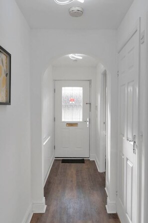 A hallway with white walls, a wooden floor, and a door with a window. - Buie`s Runway Retreat (Edinburgh)