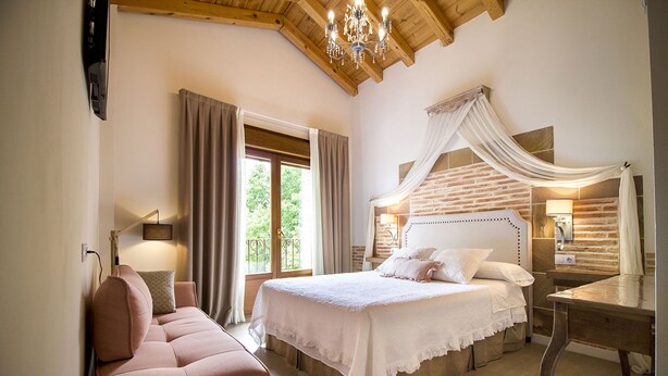Un dormitorio con cama, una silla, un escritorio y una ventana con cortinas.