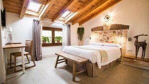 Un dormitorio con chimenea de piedra, techo de madera, una cama, un banco, un escritorio y una ventana con cortinas.