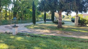 Un sendero de grava serpentea por un jardín cuidado, con árboles y un farol.