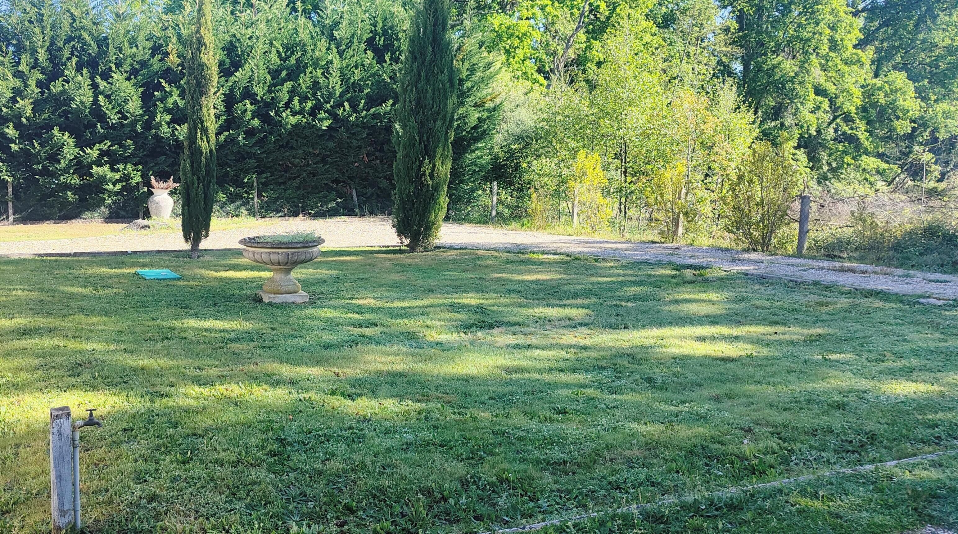 A grassy outdoor area with a stone fountain, trees, and a pathway.