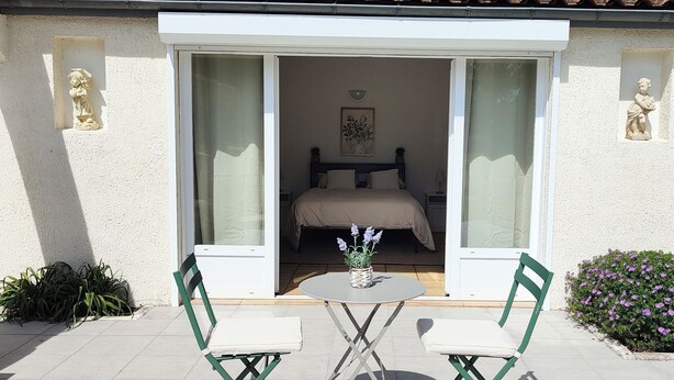Una habitación con una cama, una mesita de noche con un florero y dos sillas.