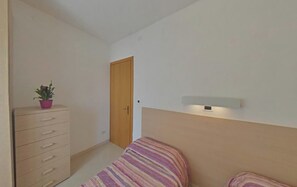 A bedroom with a bed, a dresser, a door, and a wall-mounted light fixture. - Equipped Family Flat in the Heart of Lignano (Lignano Sabbiadoro)
