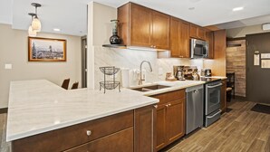 A modern kitchen with wooden cabinets, a marble countertop, a stainless steel dishwasher, and a microwave. - Slopeside Condo w/ Chairlift Views & Pool (Breckenridge)