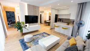 Una sala moderna con un sofá, una mesa de centro, un televisor y un comedor con sillas.