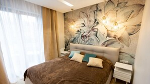 Un dormitorio con una cama grande, una mesita de noche, una lámpara de pared y un mural floral.