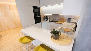 Una cocina moderna con armarios blancos, horno empotrado, cafetera y dos sillas amarillas.