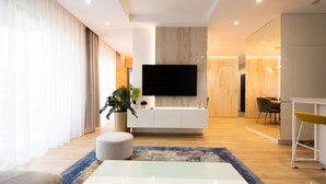 Una sala de estar moderna con televisor de pantalla plana, mueble blanco para entretenimiento, comedor y cocina.