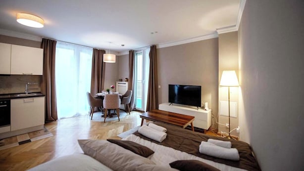 Ein Hotelzimmer mit Bett, Fernseher, Schreibtisch mit Stuhl, einer Küchenzeile und einem großen Fenster.
