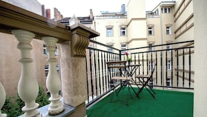 Ein Balkon mit Teppich im Grünton, einem Holztisch und -stühlen sowie einem Geländer aus schwarzem Metall.