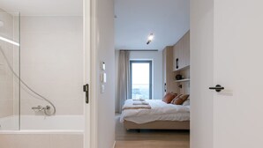 A modern bedroom with a shower, a bed with pillows, a window, and a view. - Luxury Seaview Stay With Free Private Parking (Ostend)