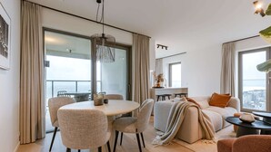 A modern living room with a dining area, large windows, and a view of the city. - Luxury Seaview Stay With Free Private Parking (Ostend)