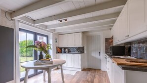 Una cucina con mobili bianchi, un tavolo di legno e vista attraverso una porta vetrata.
