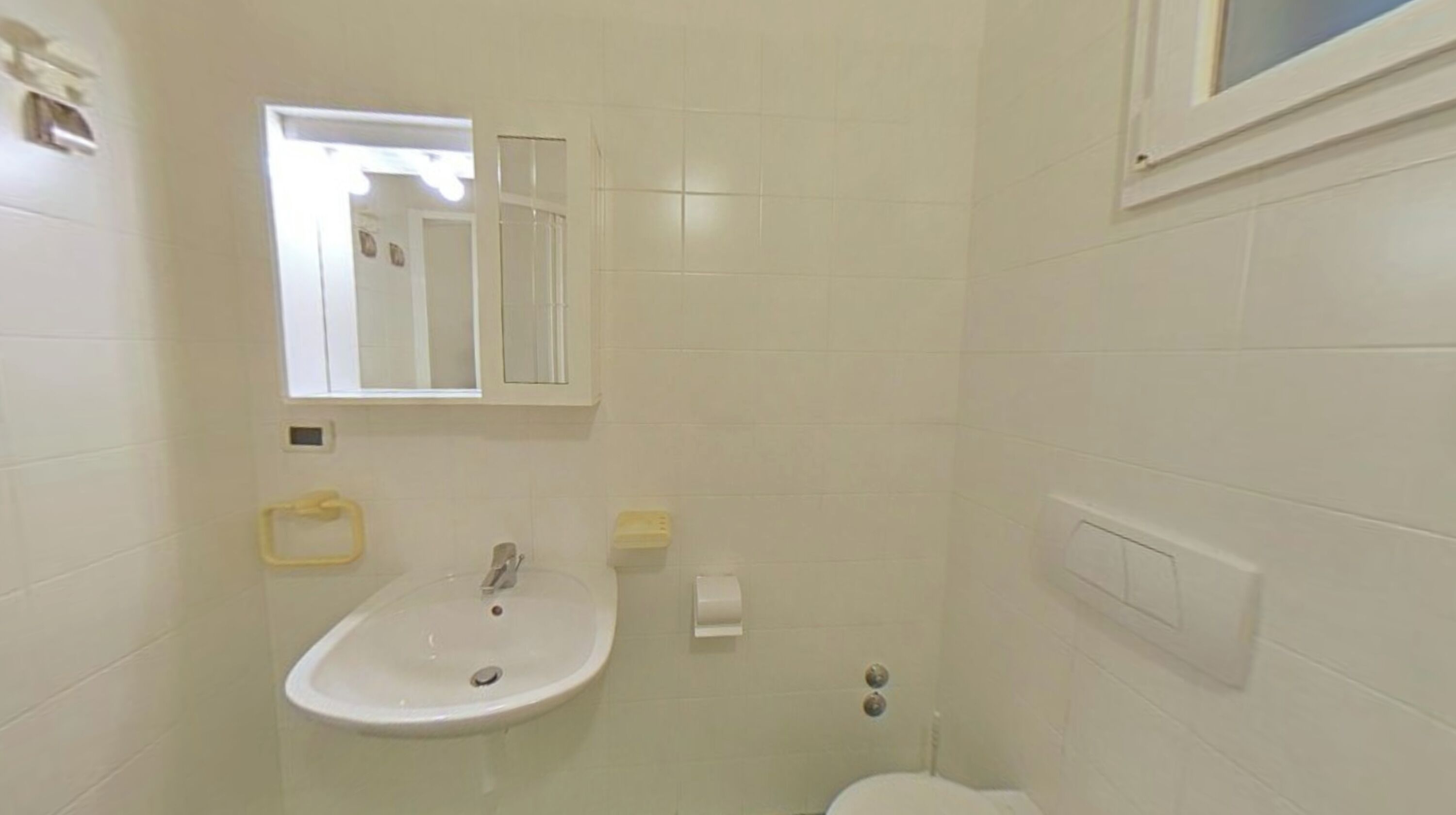 Een badkamer met een wastafel, spiegel, toilet en raam.