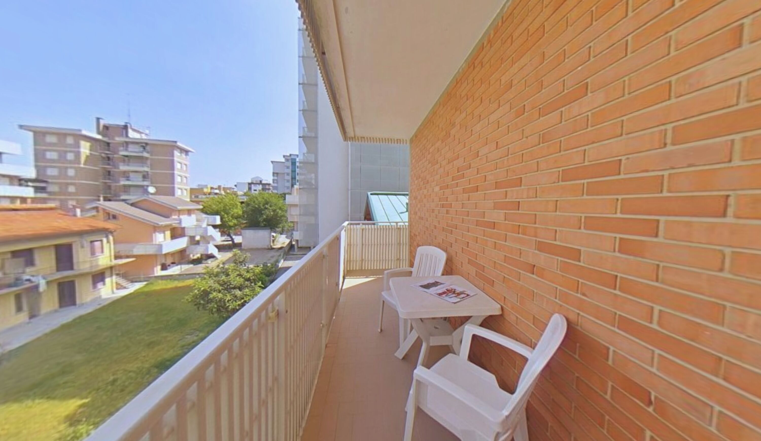 A balcony with a table and chairs, a brick wall, and a view of surrounding buildings.