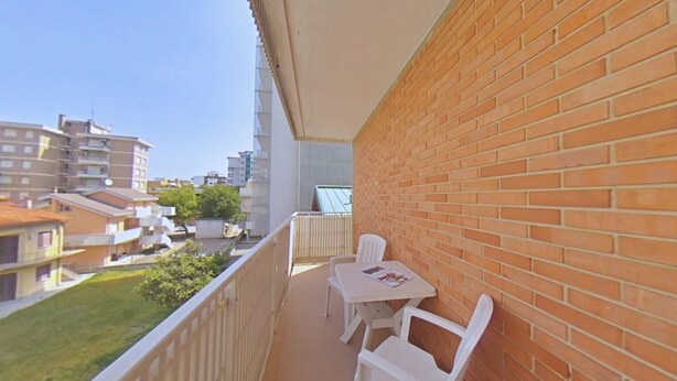 Ein Balkon mit einer Ziegelwand, zwei weißen Stühlen und einem Tisch.