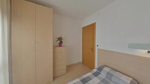 Ein Schlafzimmer mit Bett, Schrank, Schminktisch, einer Tür und einem kleinen Topf mit Pflanze.