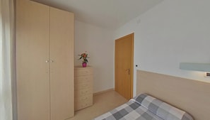 Ein Schlafzimmer mit Bett, Schrank, Schminktisch, einer Tür und einem kleinen Topf mit Pflanze.