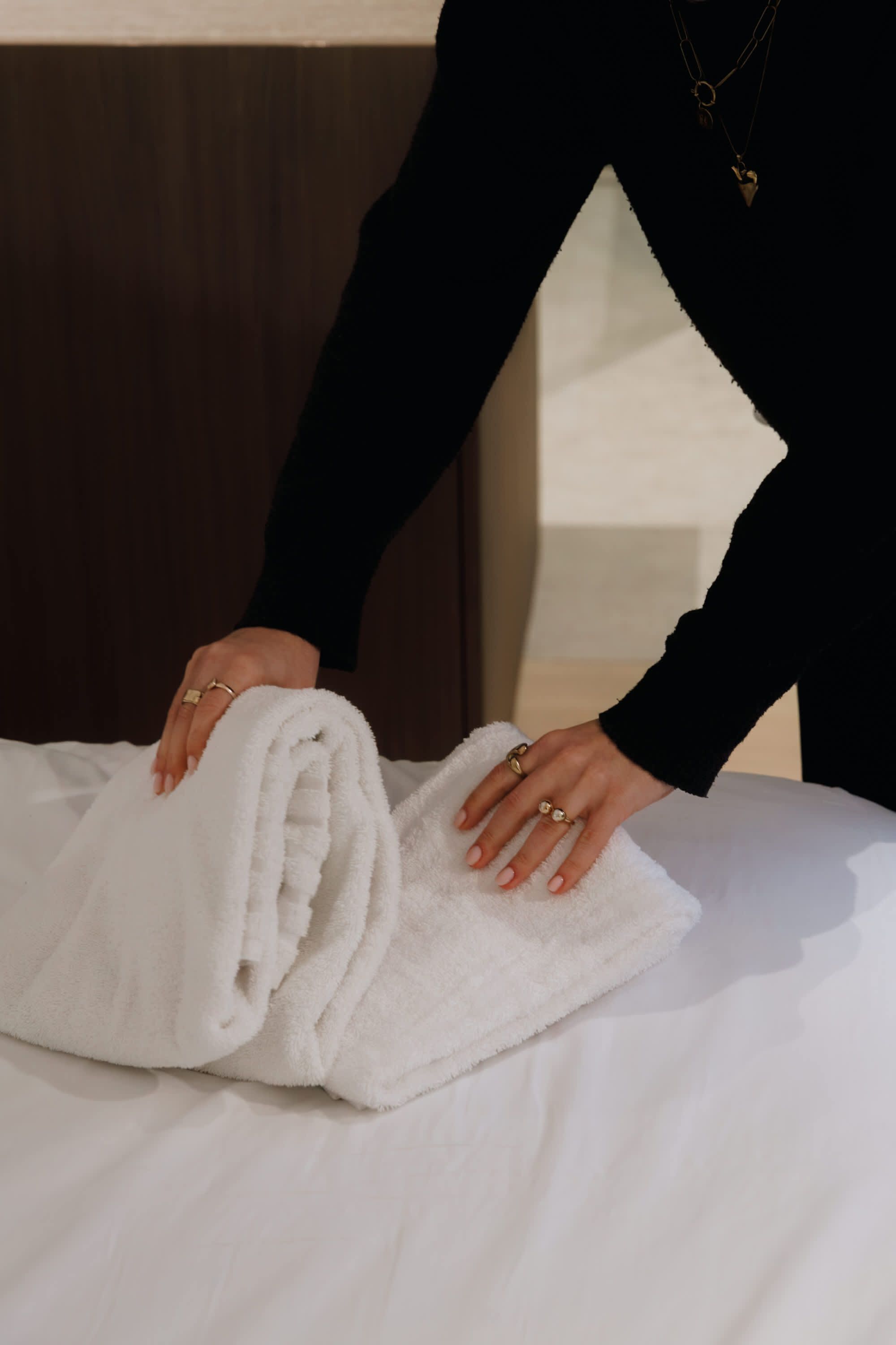 A person folding a white towel on a bed with a wooden headboard.