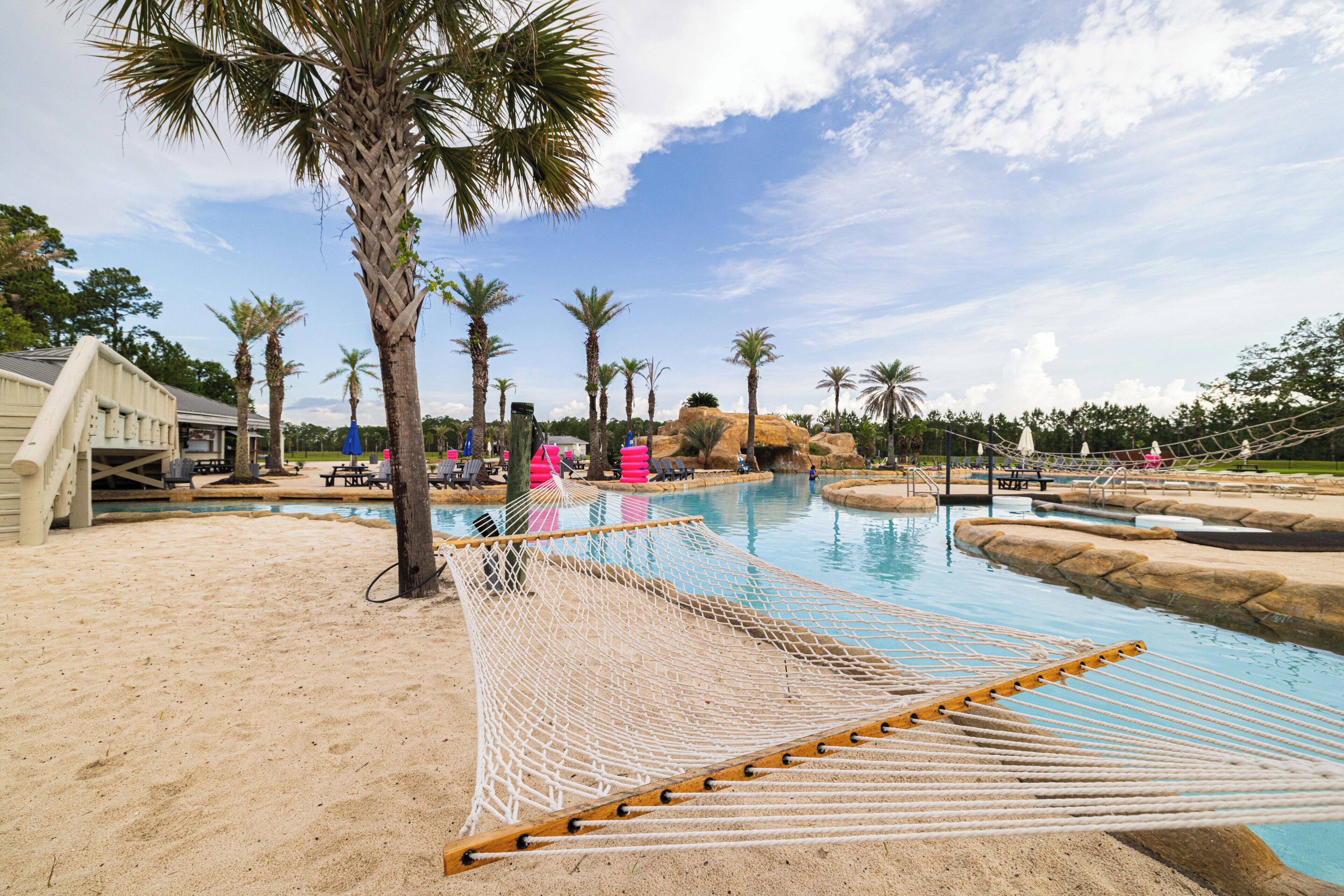 Uima-allasalue, jossa on riippumatto, palmuja ja taustalla näkyvä rakennus.