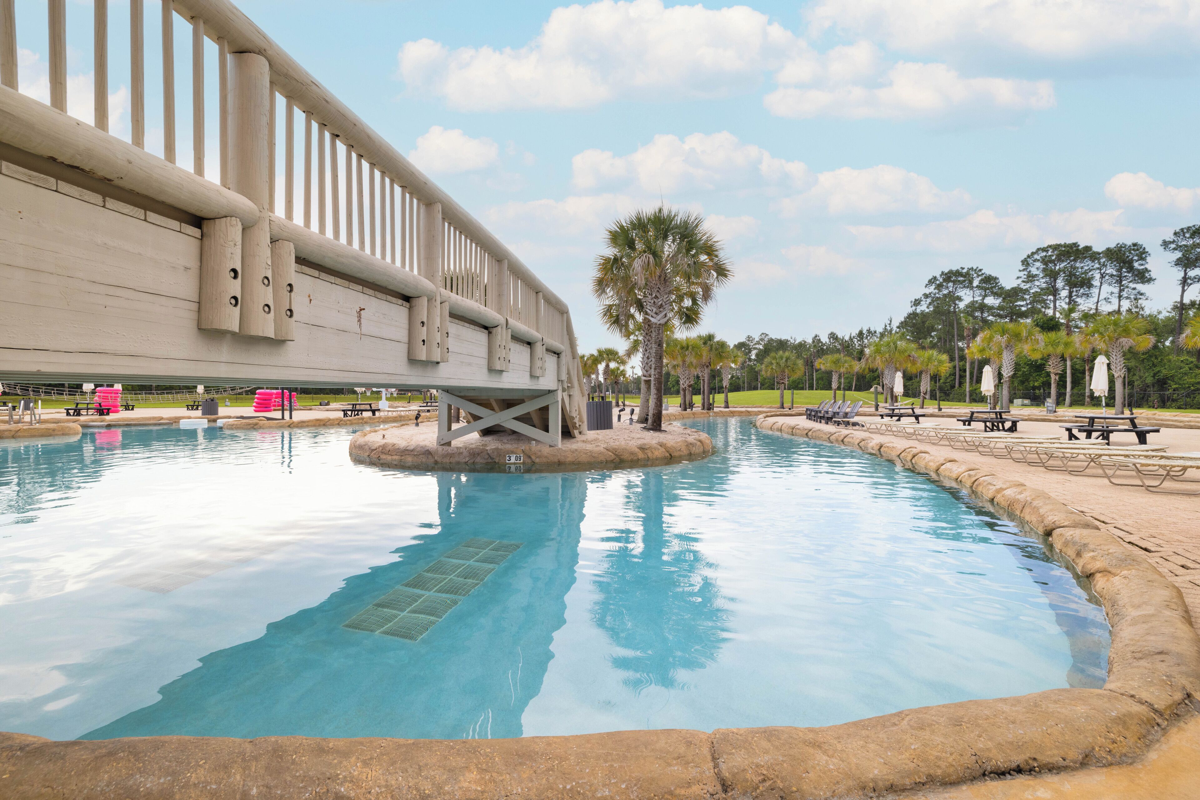 A swimming pool with a wooden deck and palm trees in the background.