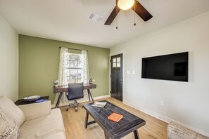 Ein Wohnzimmer mit Sofa, Couchtisch, Schreibtisch mit Stuhl, Fernseher und Deckenventilator.