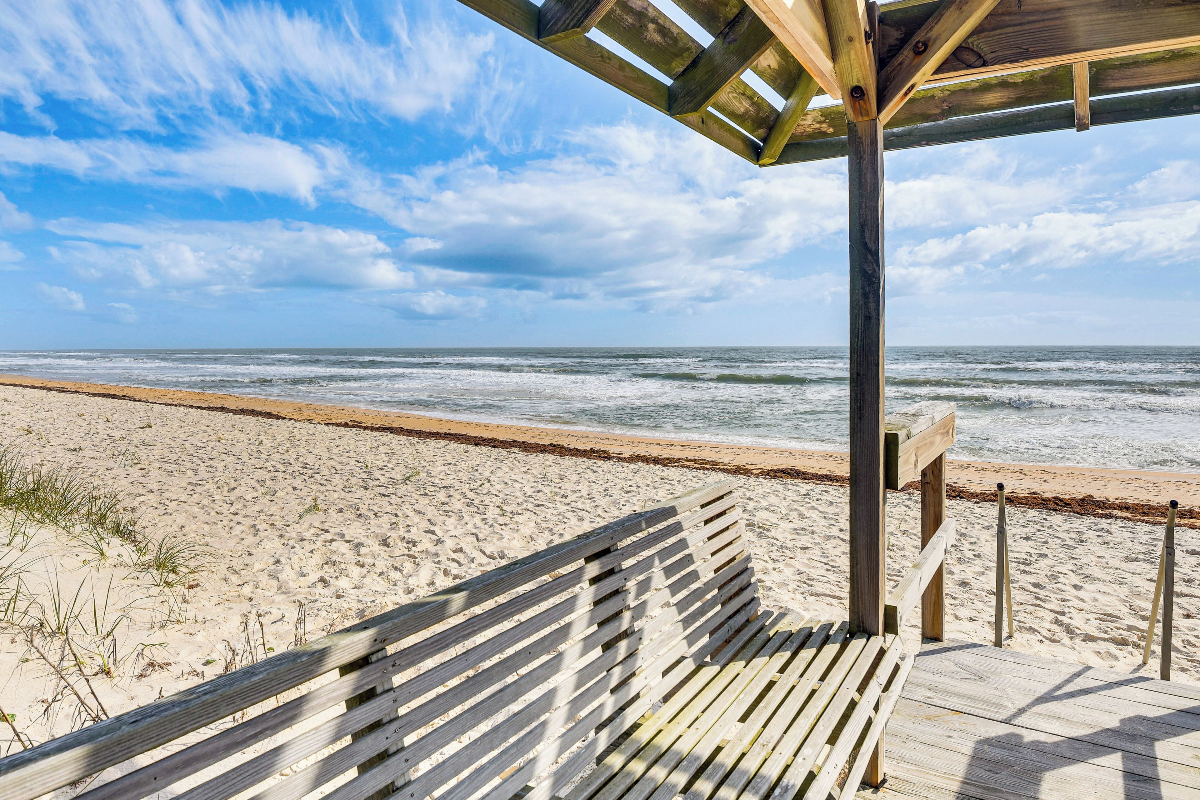A wooden bench on a wooden deck overlooking a beach with waves.
