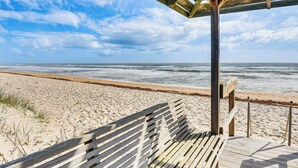 Una panchina di legno su un pontile di legno con vista su una spiaggia e le onde.