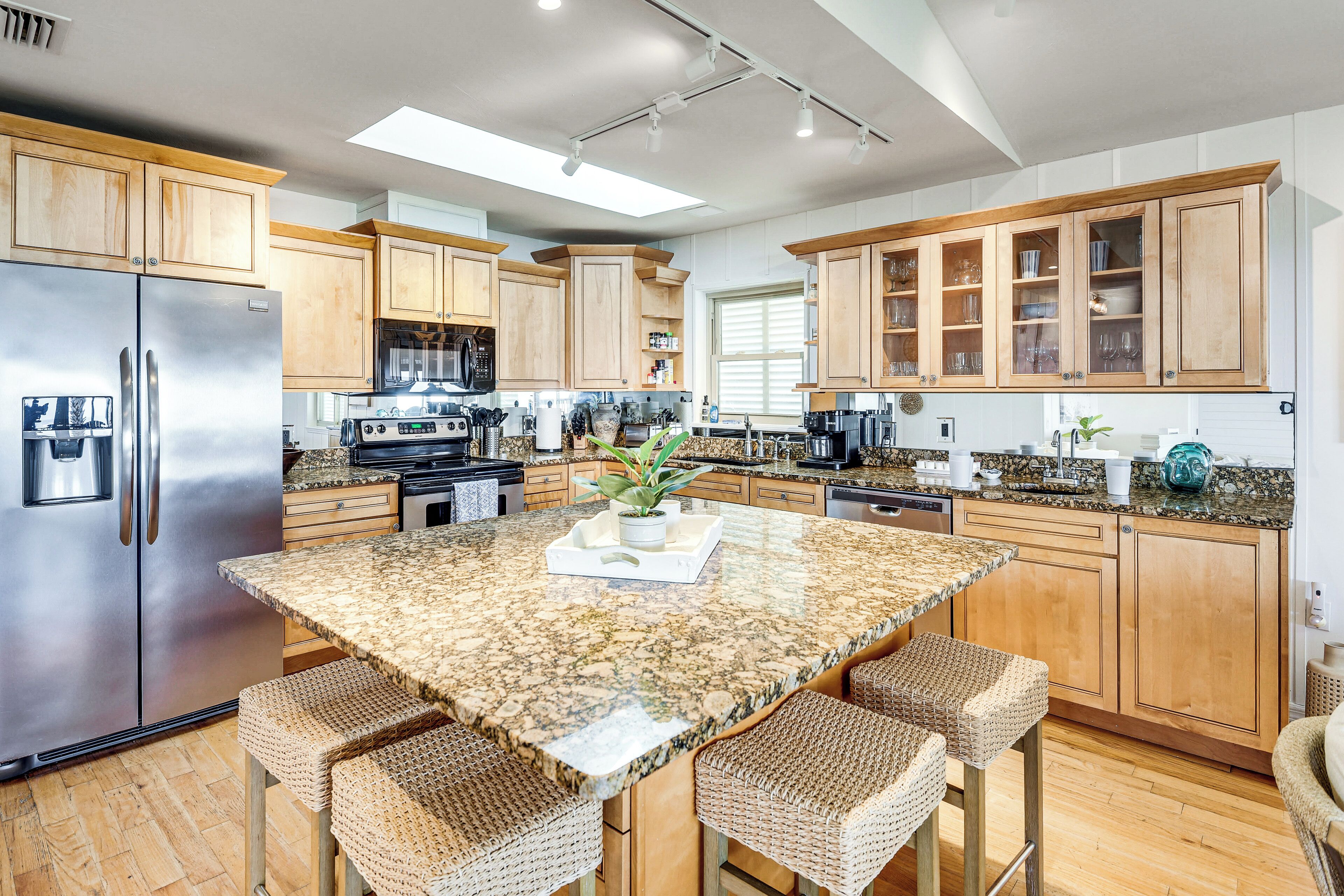A modern kitchen with wooden cabinets, a granite countertop, a stainless steel refrigerator, and a central island with bar stools.