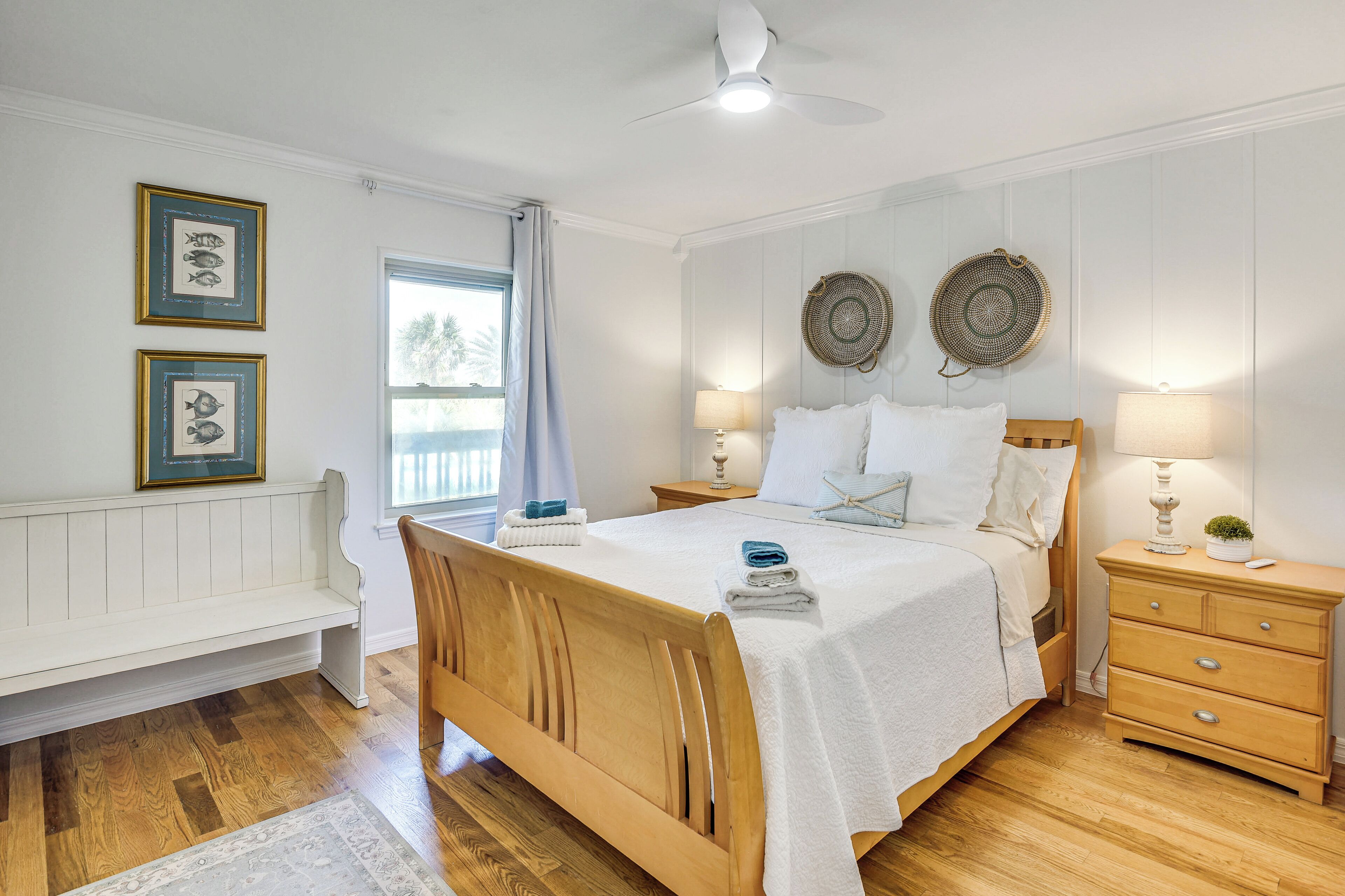 A bedroom with a wooden bed, white walls, a bench, two wall-mounted lamps, and a ceiling fan.