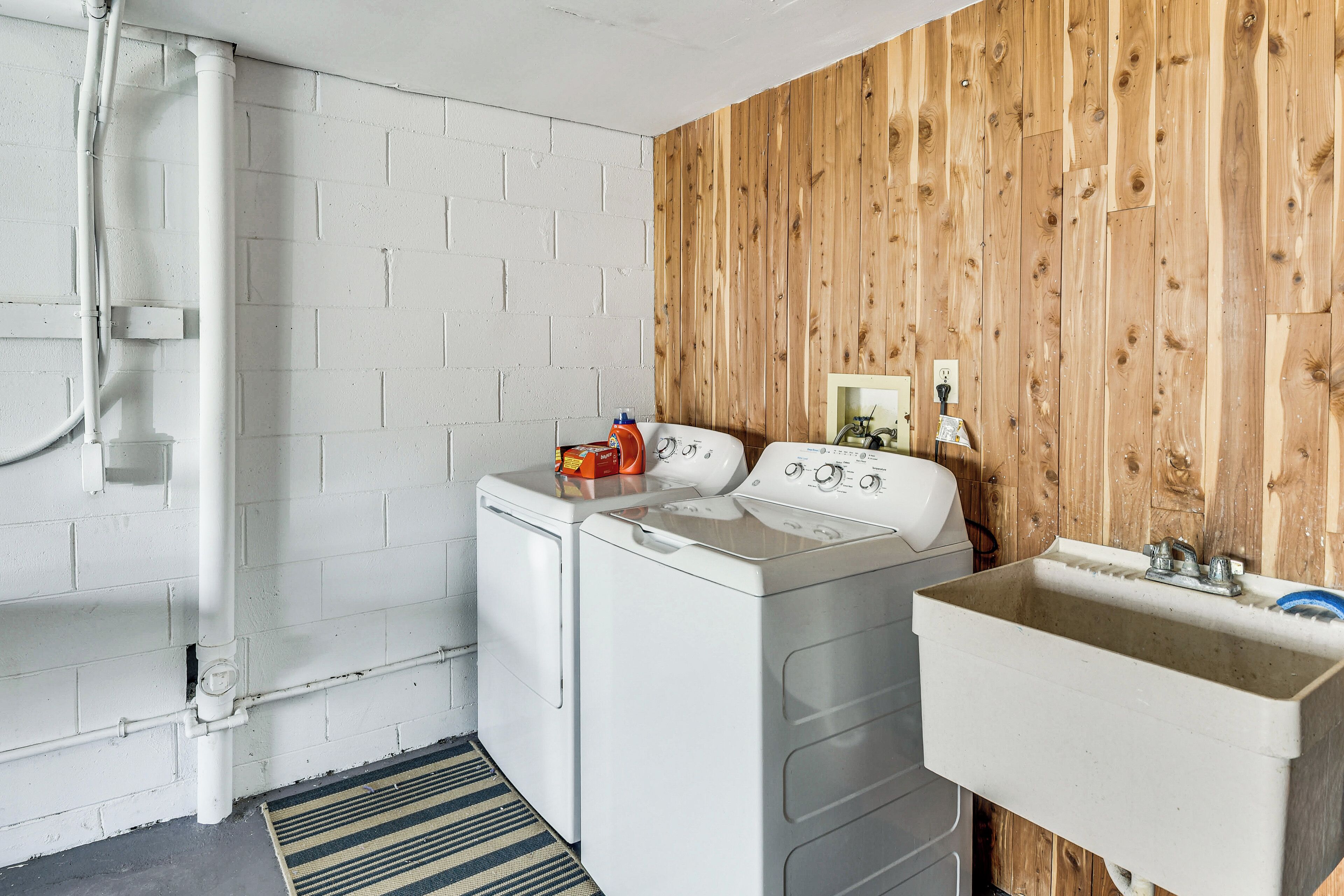 A laundry area with two white washing machines, a sink, and a wooden wall.