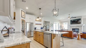 A modern kitchen with a central island, wooden cabinets, stainless steel appliances, and a fireplace. - Steps From the Water! Grand Lake Getaway w/ Patio (Afton)